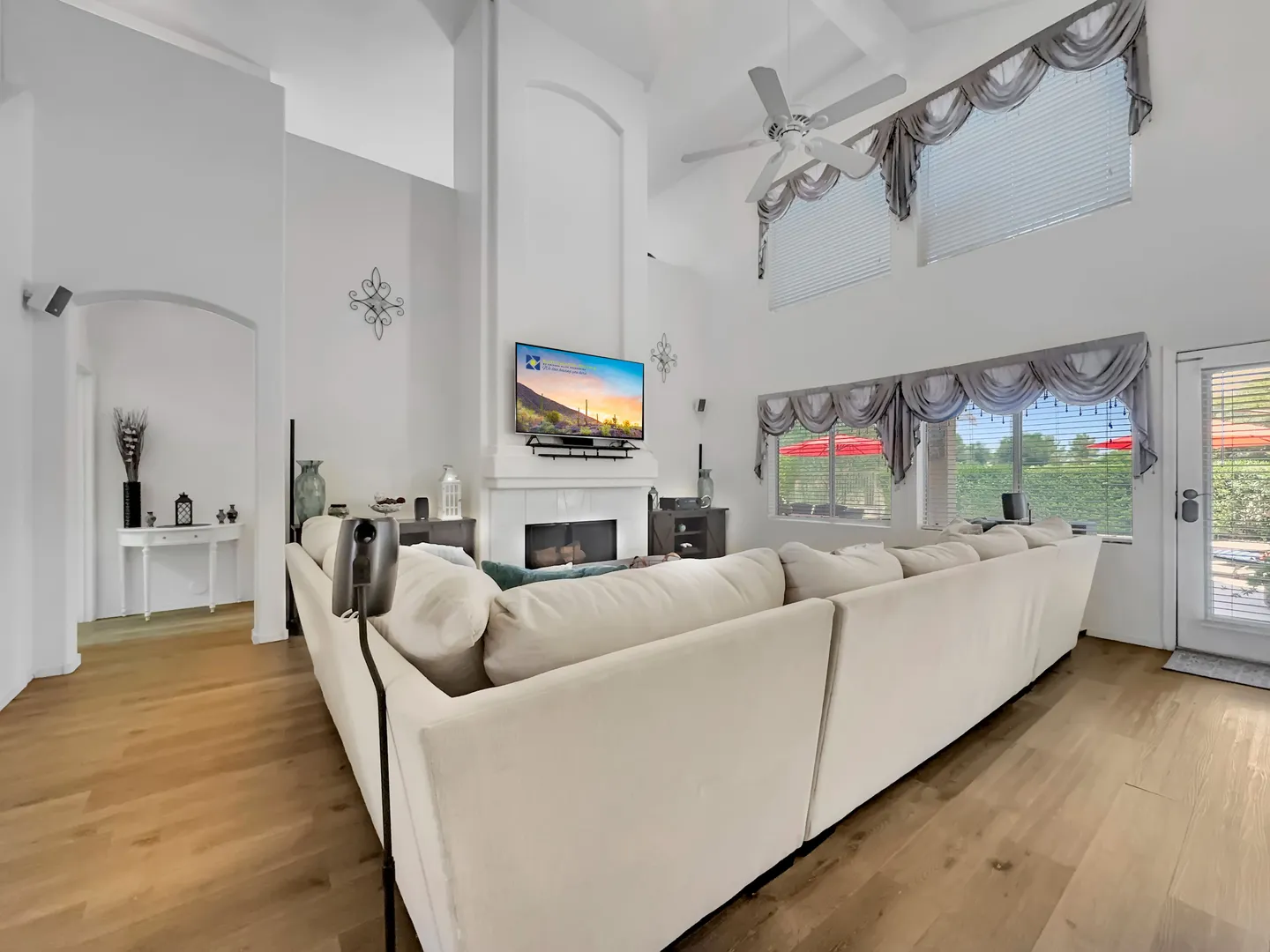 Bright family room with a large sectional sofa, fireplace, wall-mounted TV and high ceilings