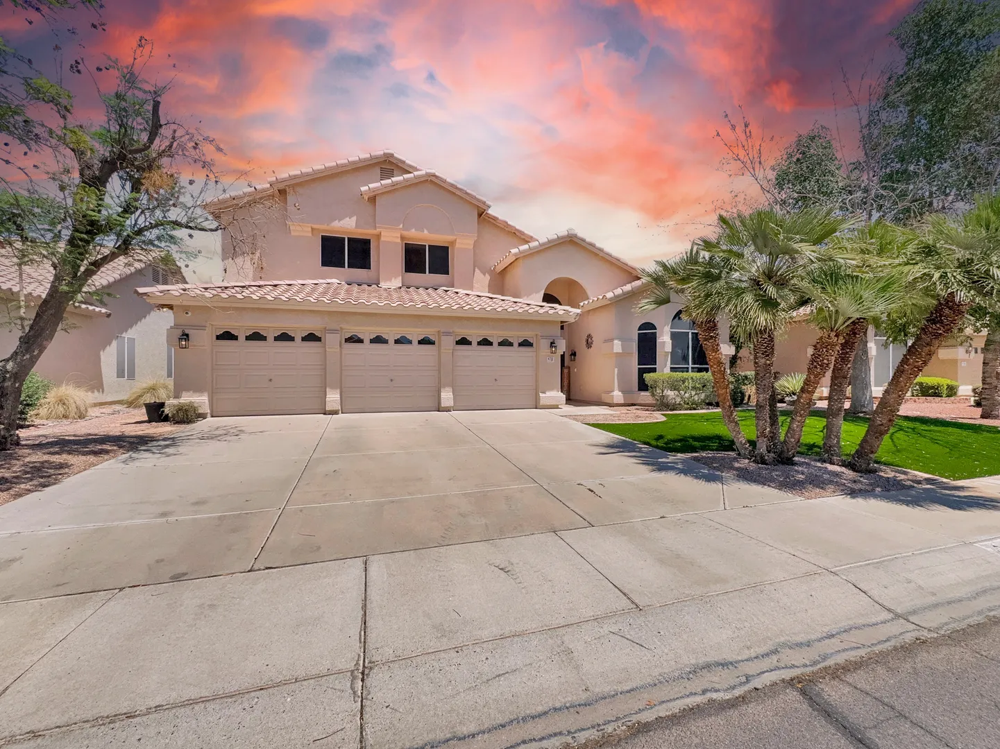 Front of the two-story stucco home with a tile roof, three-car garage, wide driveway and palm trees