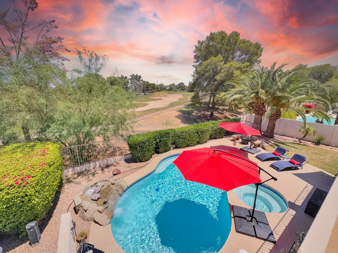 Aerial view of the backyard pool and spa with red umbrellas and loungers, backing onto the green golf course at sunset